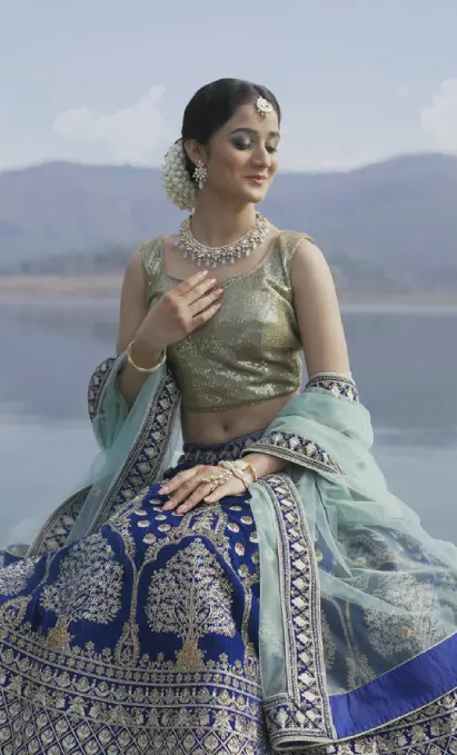 A beautiful Indian Bride wearing a beautiful blue intricate lehenga on a boat with a beautiful water background.